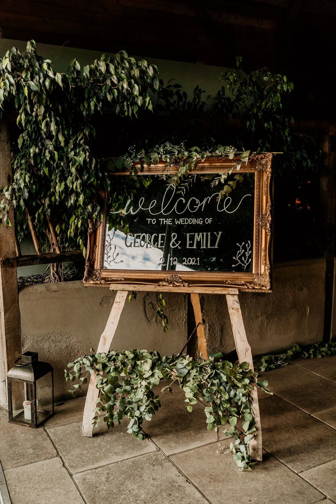 Rustic wedding welcome signs with names and greenery decorations displayed on wooden easels.
