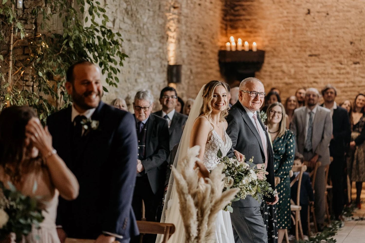 Wedding ceremony in rustic brick venue with string lights and greenery decorations.
