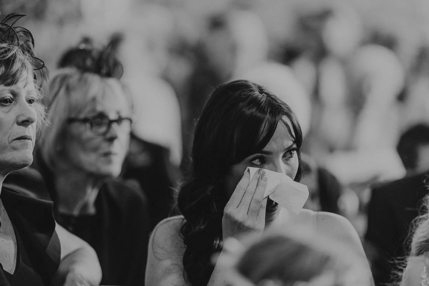 Black and white shot of wedding guests watching an emotional ceremony moment.