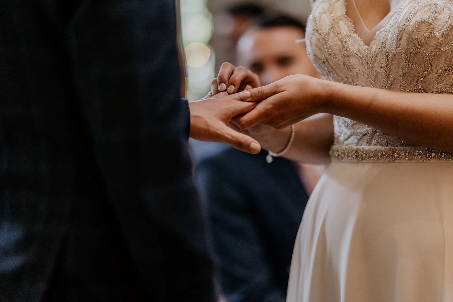 Close-up of wedding ceremony details showing hands and elegant lace dress details.