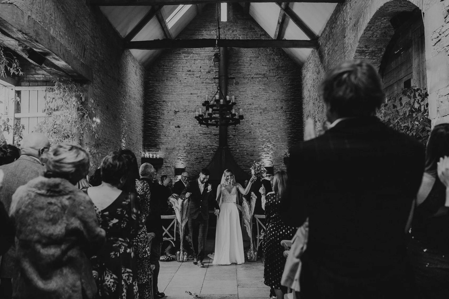 Wedding guests gather inside a historic stone barn venue with exposed beam ceiling.