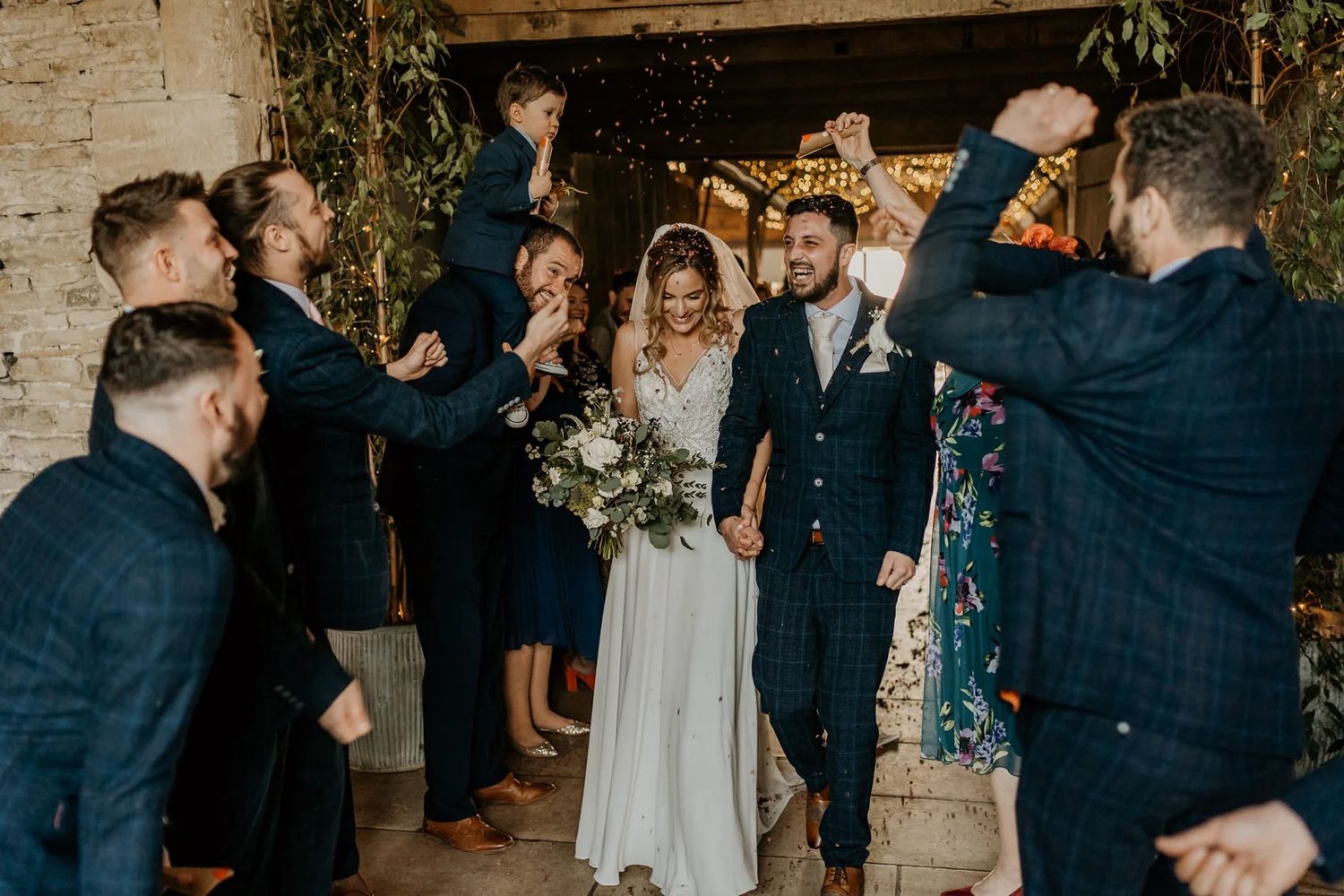 A wedding celebration in a rustic venue with guests cheering as newlyweds beam with joy under string lights.