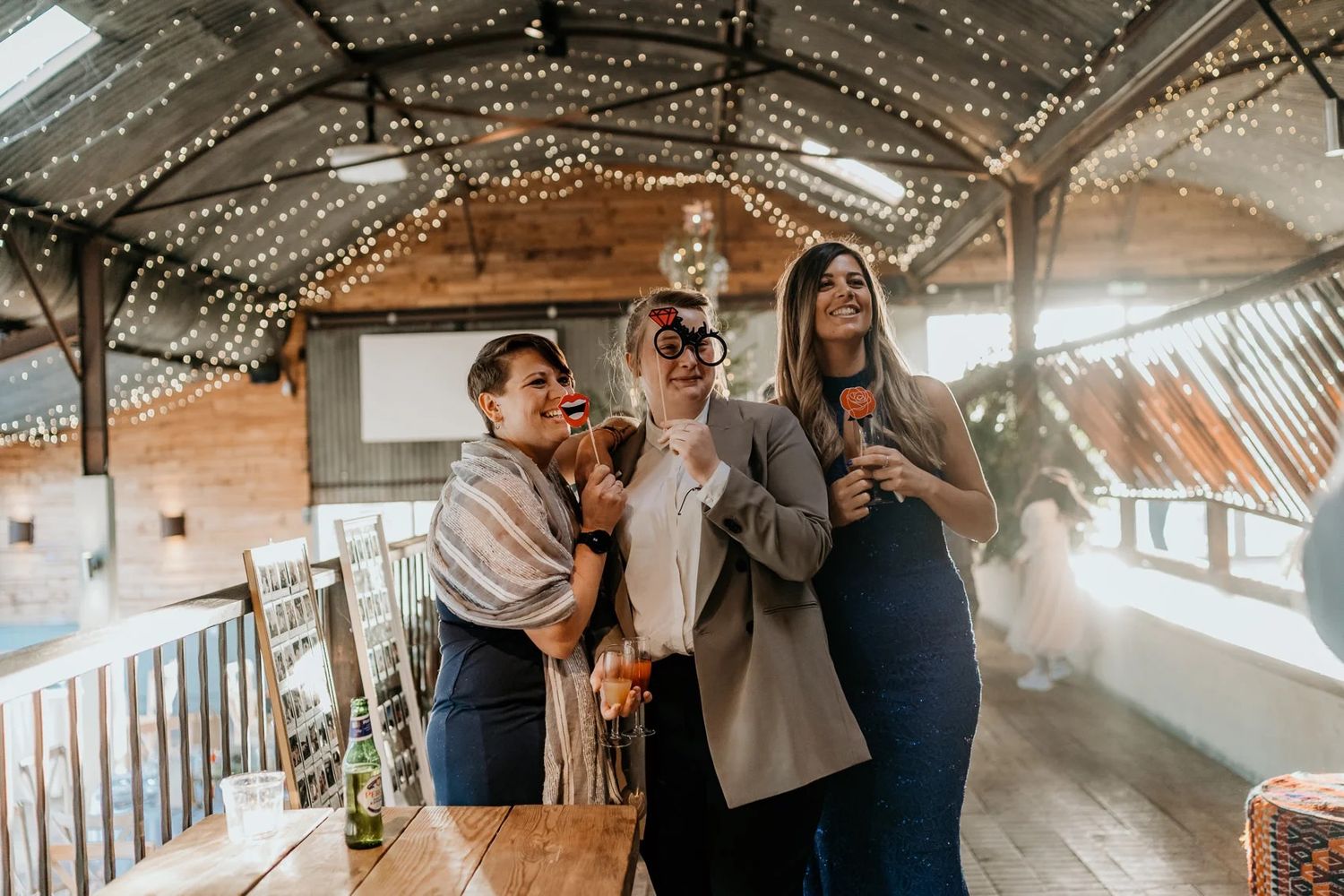 String lights illuminate a rustic barn wedding venue with exposed wood beams and white decor.