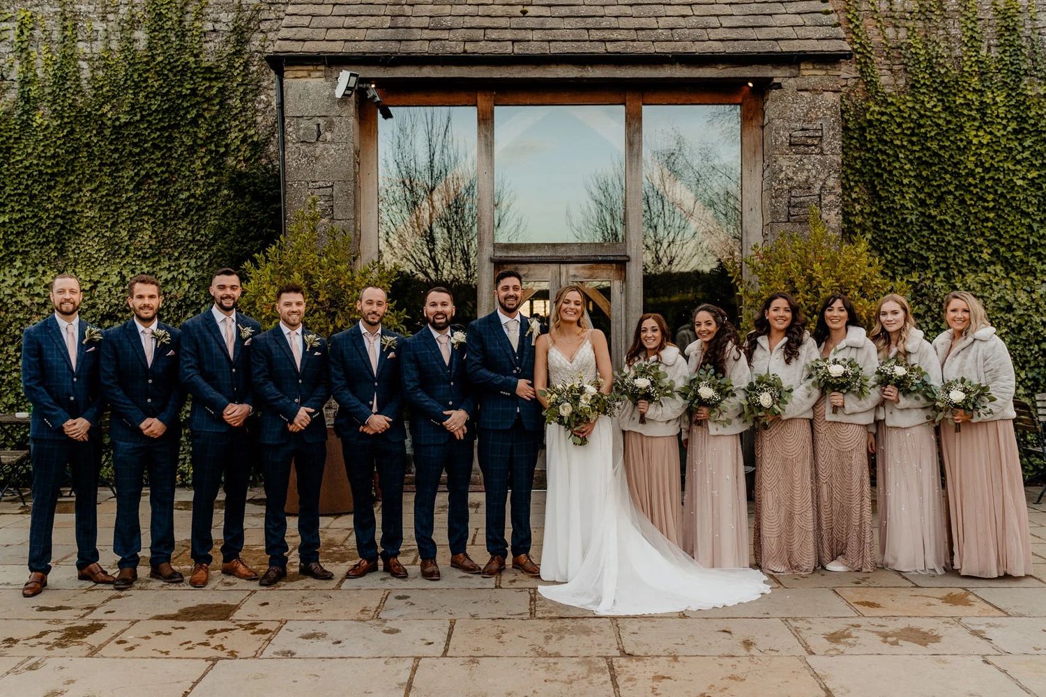 Wedding party stands in front of rustic barn while posing for formal group photos in various arrangements.