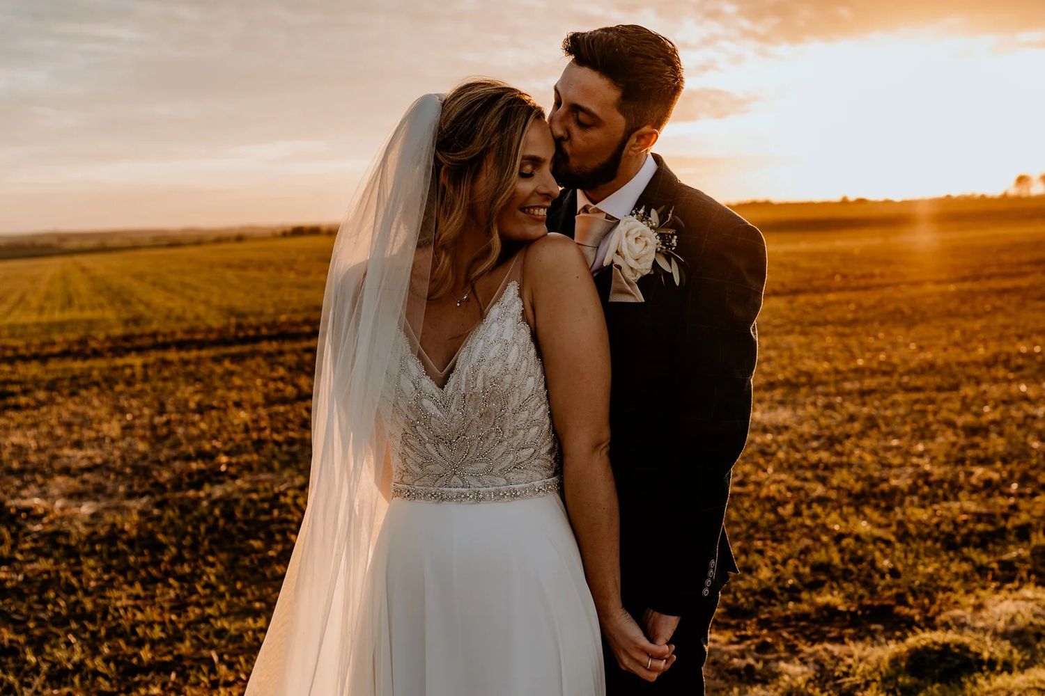 Romantic silhouettes embrace against a golden sunset over a vast rural landscape during an intimate countryside wedding.