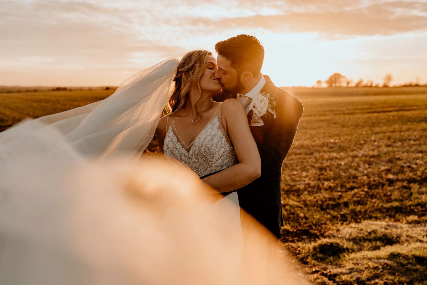 Couple walking in a golden field at sunset creating a romantic silhouette against the warm sky.