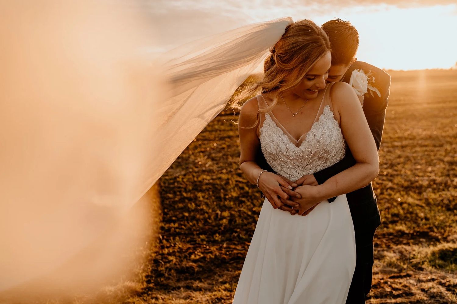 Newlyweds share an intimate moment in a meadow bathed in warm sunset light.