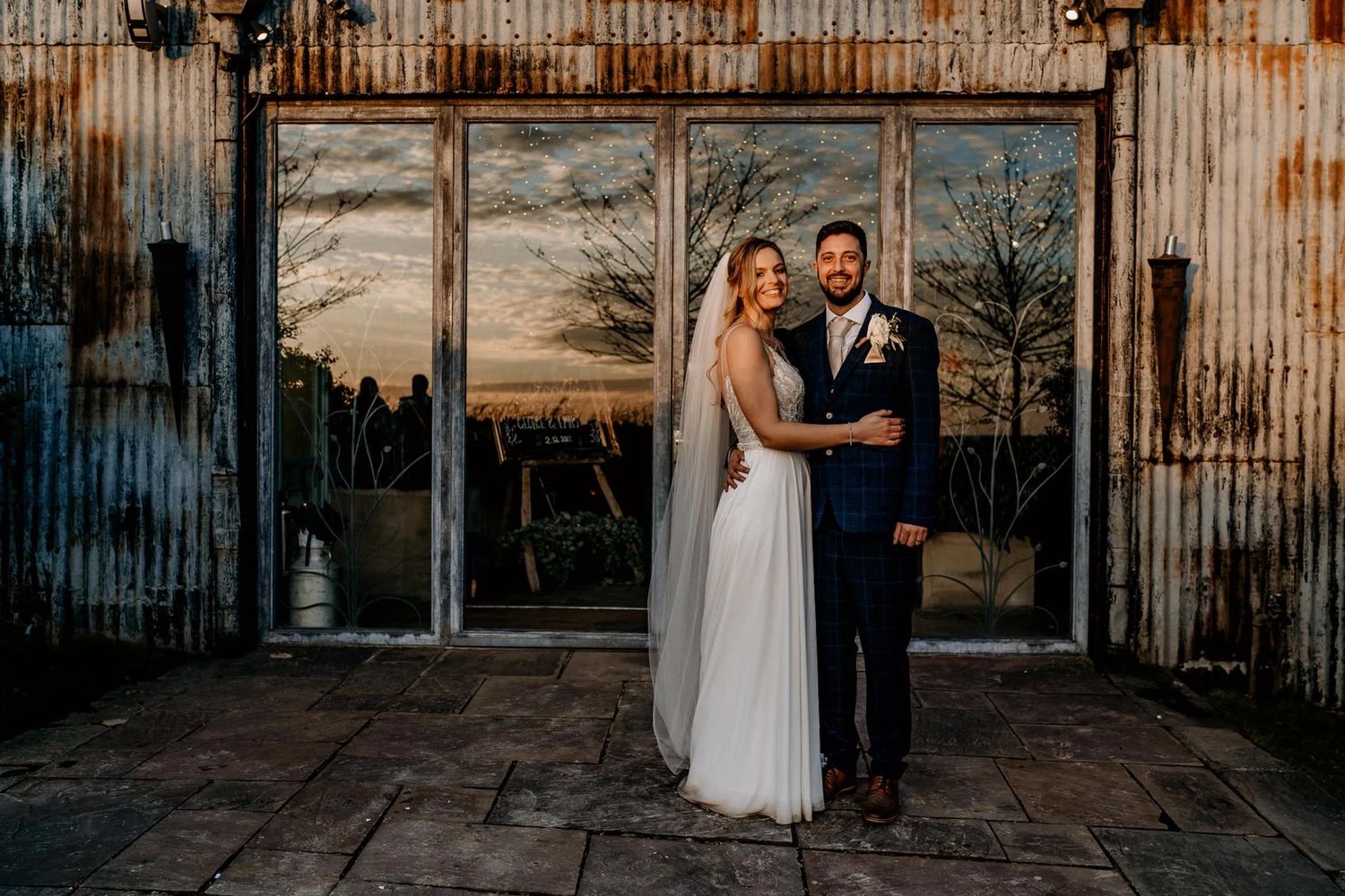 Couple celebrates their wedding day against a rustic metal wall backdrop at sunset.