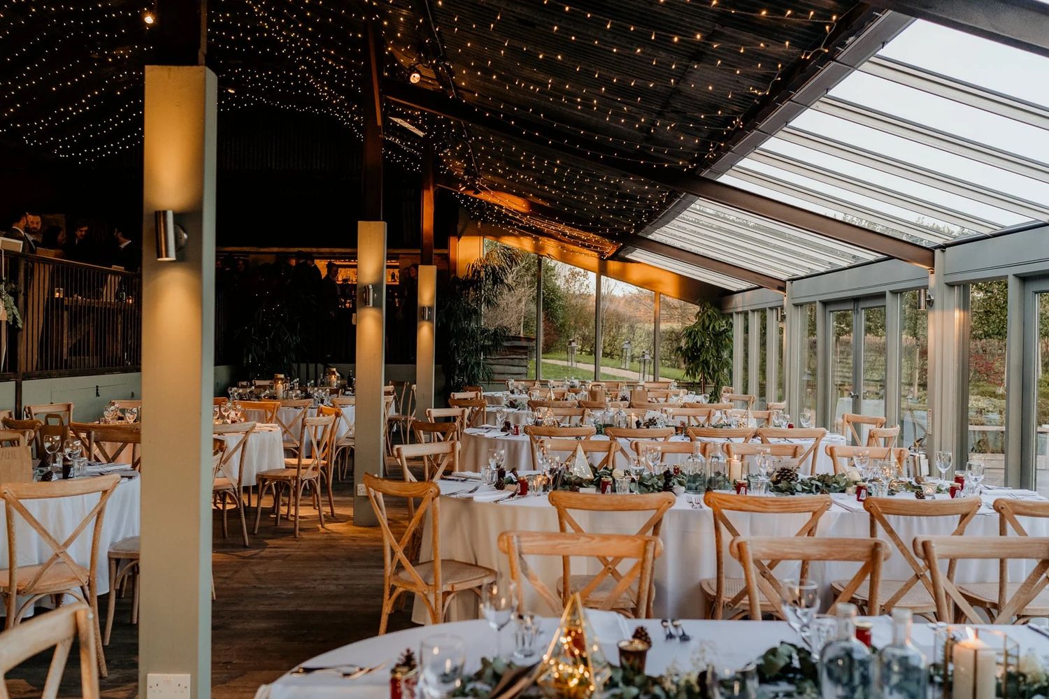 A modern wedding reception venue with cross-back chairs and elegant place settings arranged under skylights.