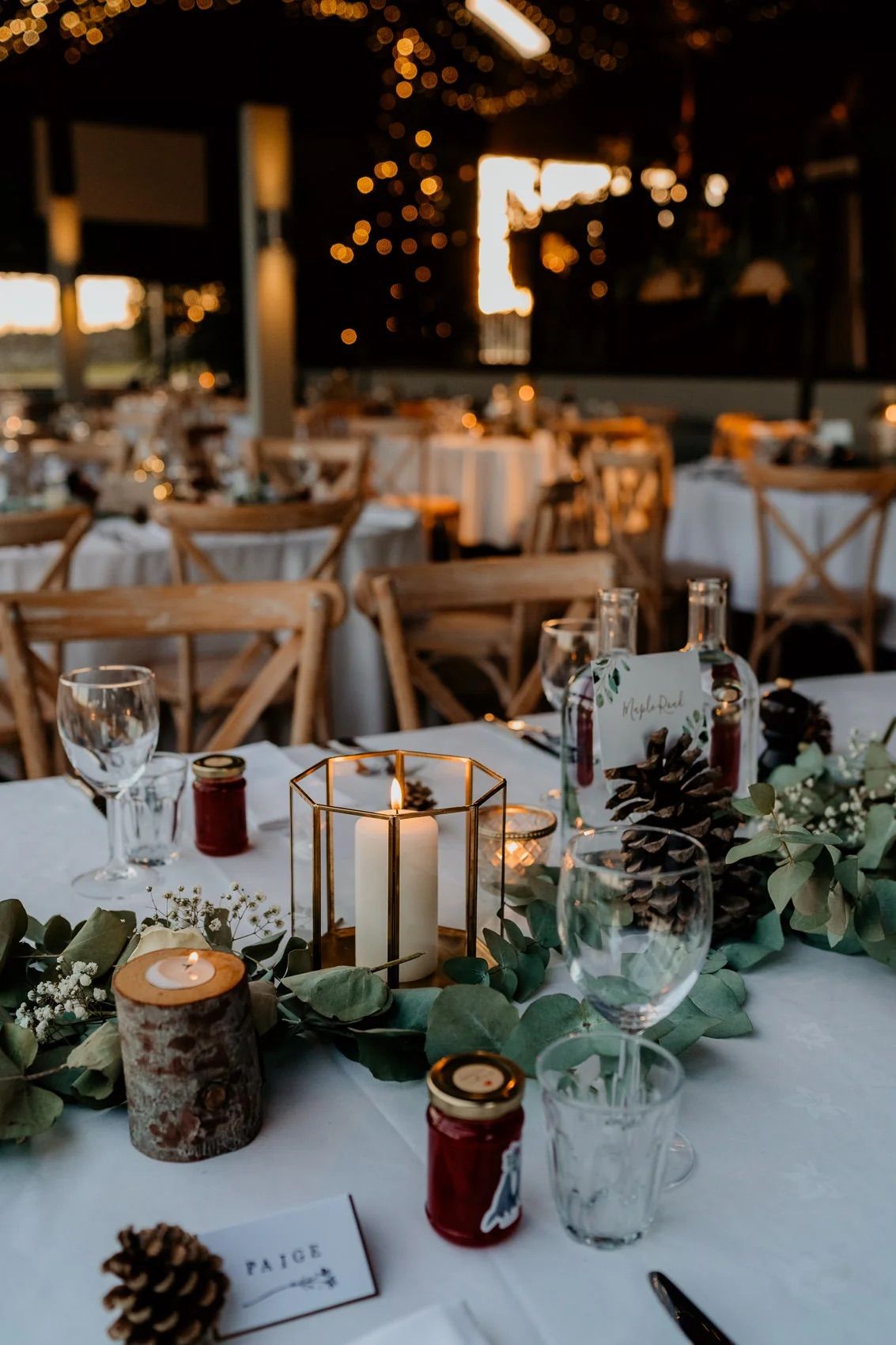 Rustic wedding table decor with wooden candle holders, pine cones, and greenery on white linens.