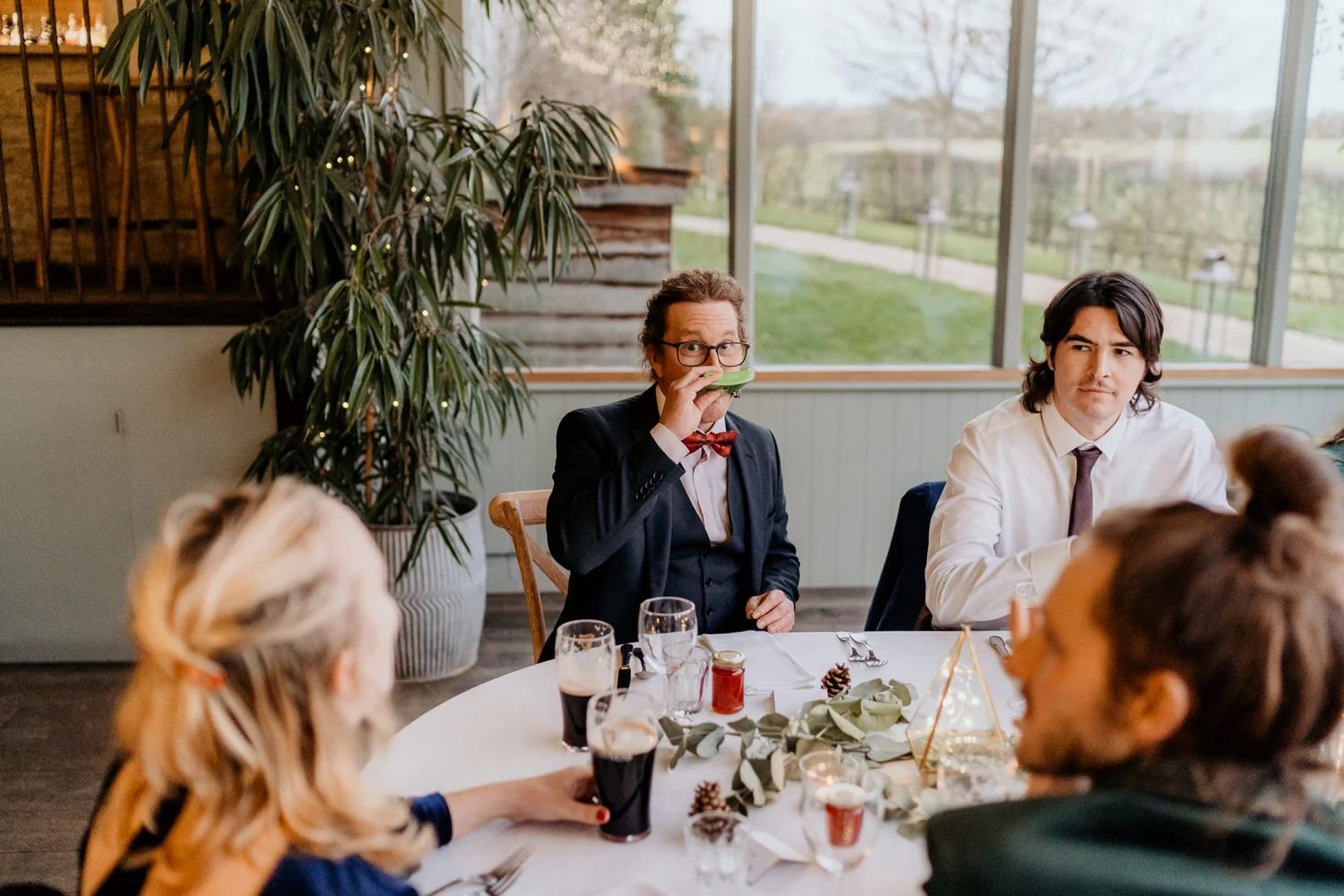 A group of people sitting at a long table in a bright restaurant setting during a casual gathering.