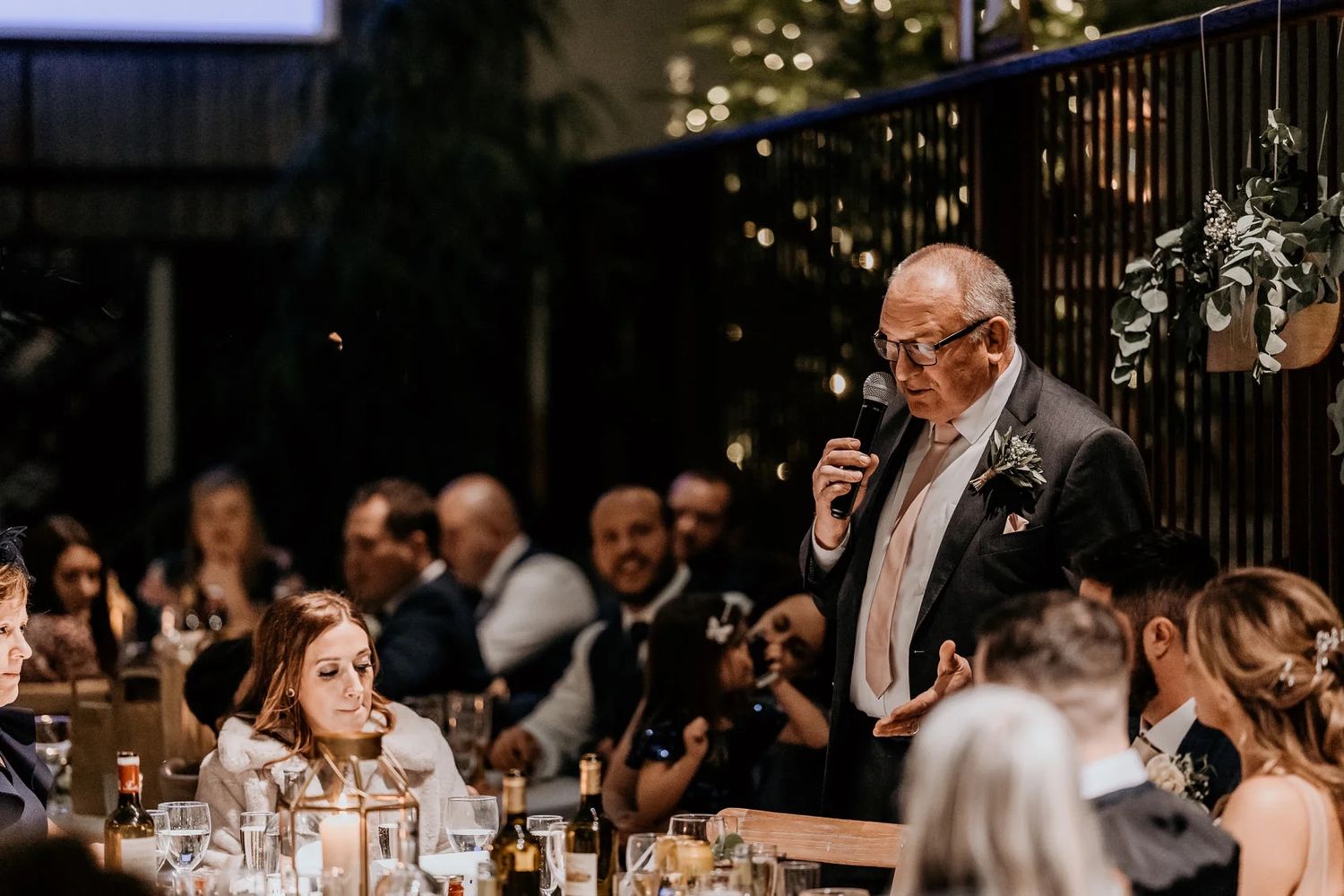 Wedding guests gathered around dinner tables during an evening reception with warm lighting and festive atmosphere.