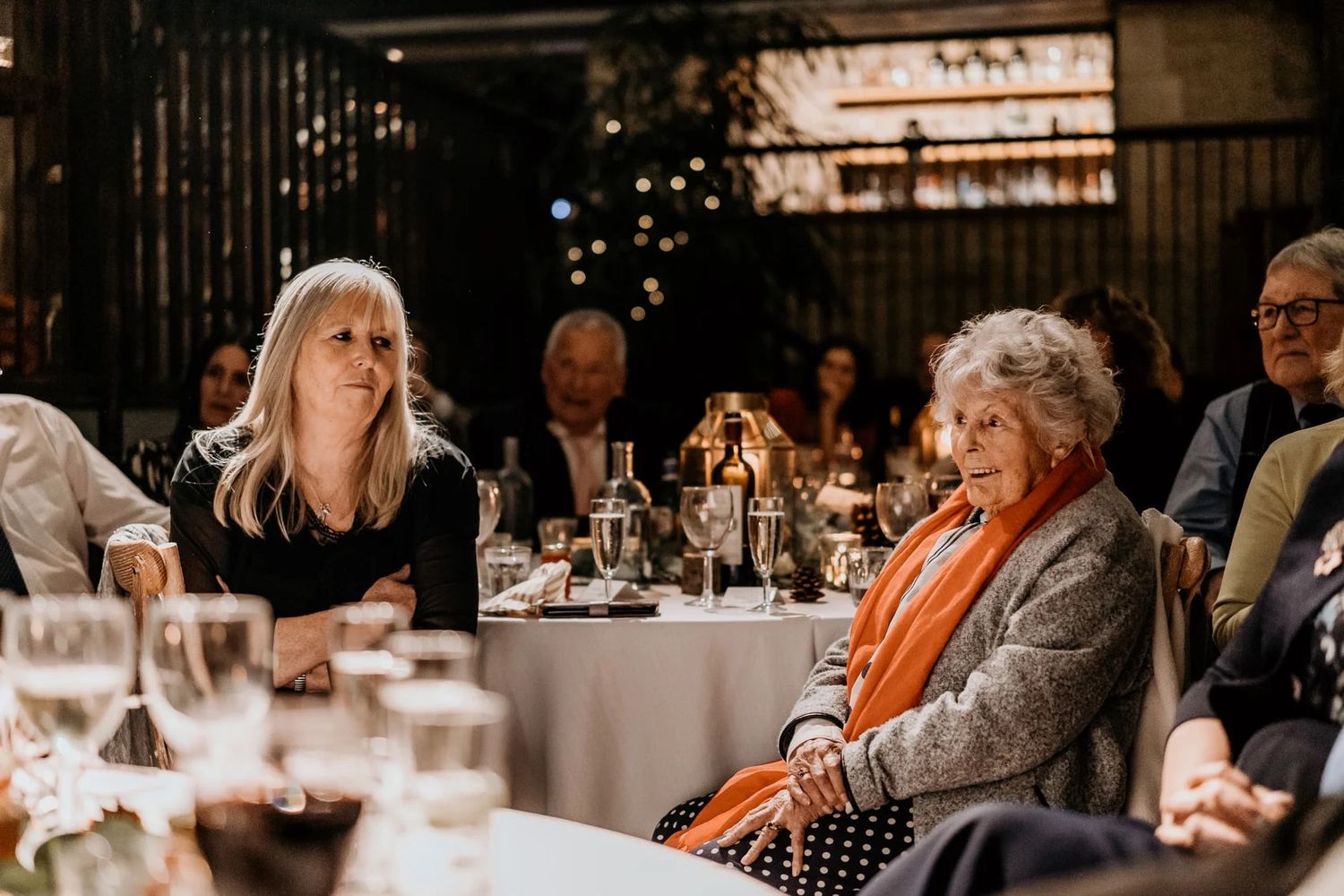 Wedding reception dinner in a rustic venue with elegant table settings and warm ambient lighting.