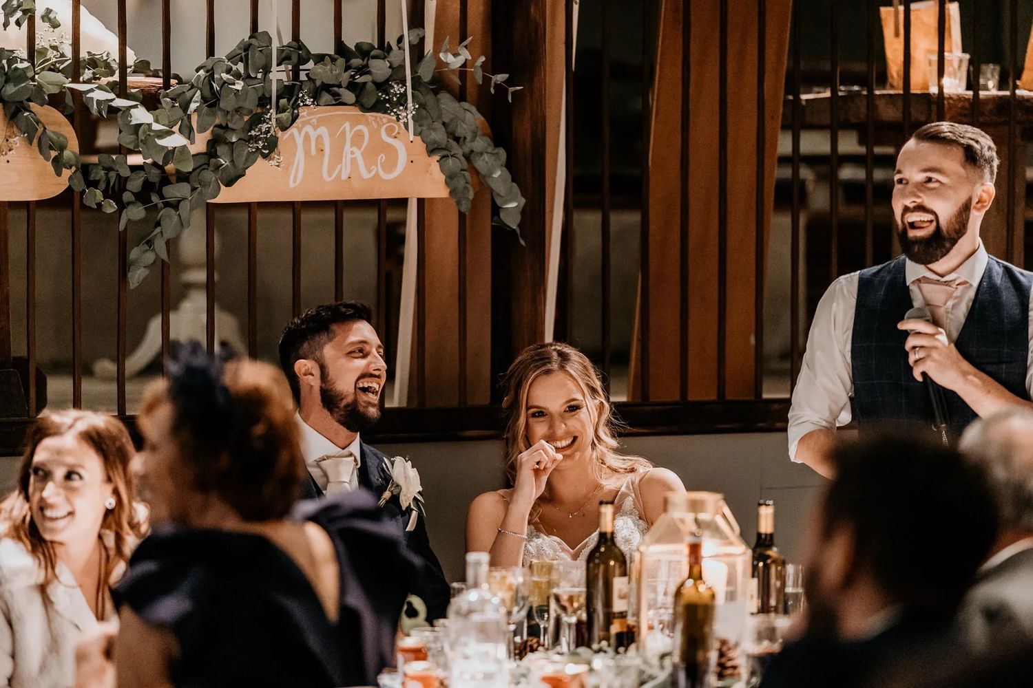 Wedding reception venue decorated with warm lighting and guests gathered at long dining tables.