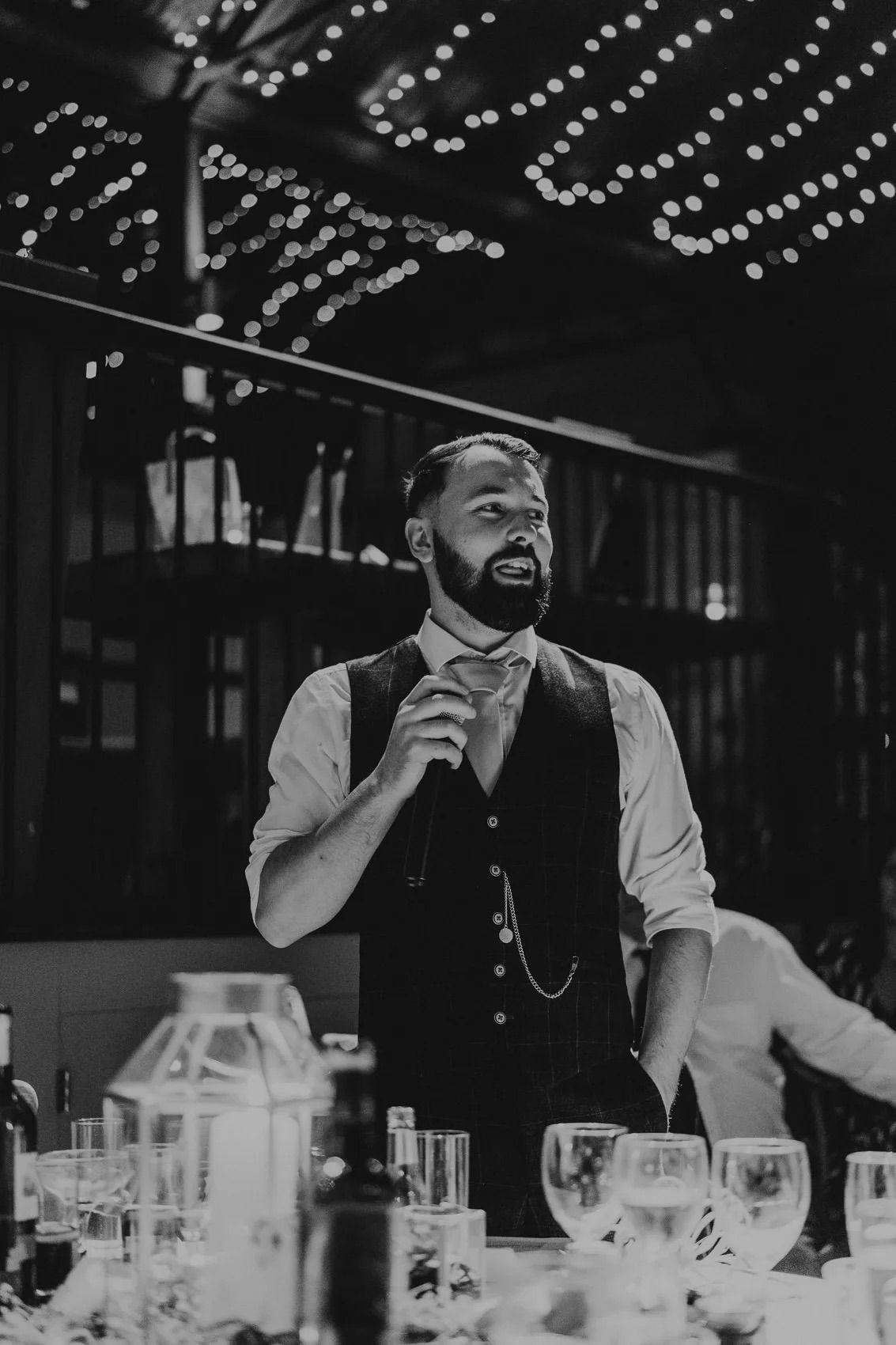 Black and white image of waitstaff in vests working behind tables at an elegant event.