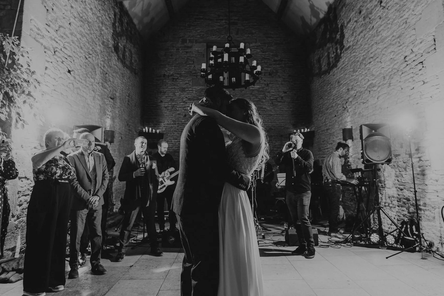 Wedding guests dancing and celebrating at a rustic stone venue with string lights overhead.
