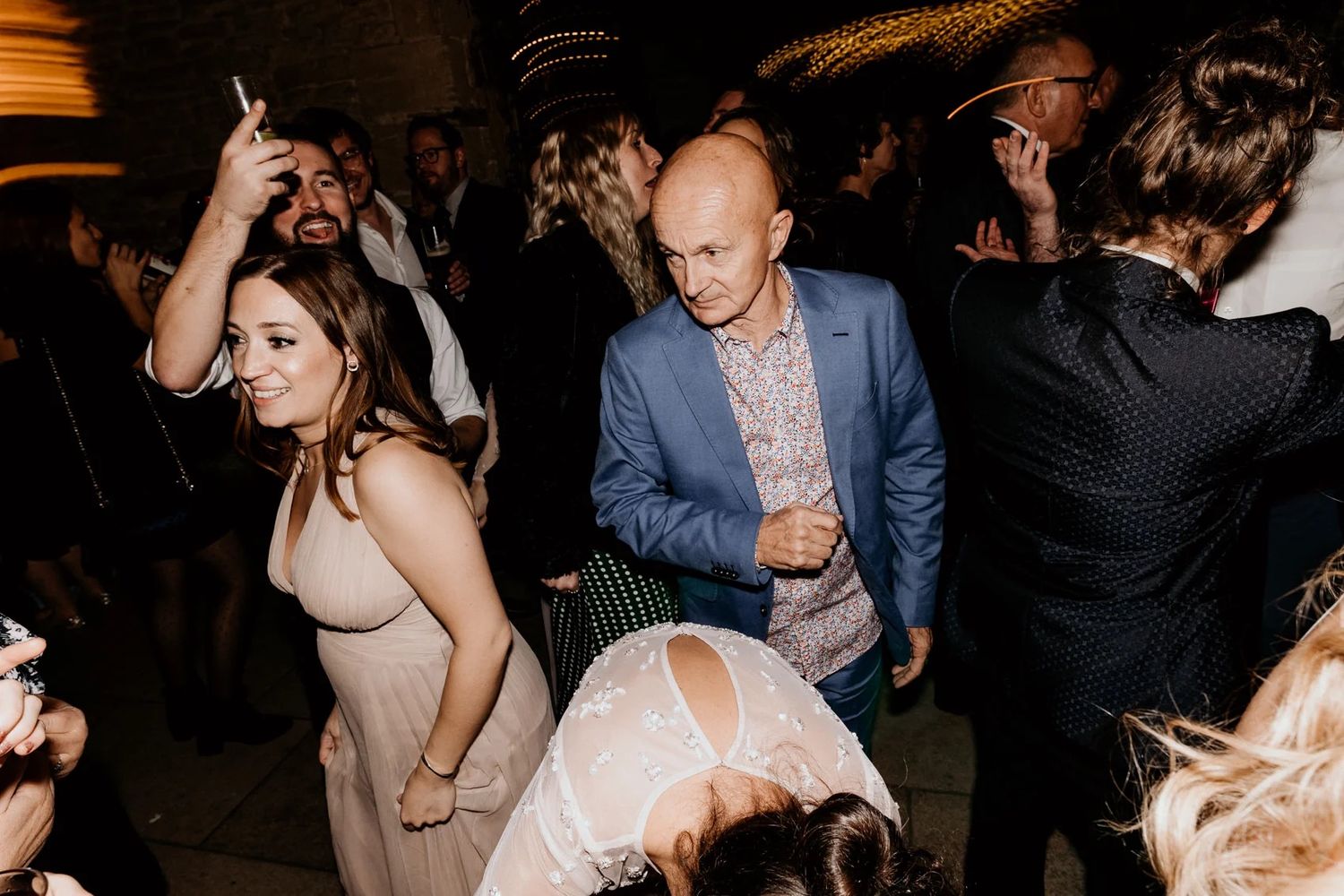 Wedding reception dance party with guests enjoying themselves under ambient lighting.