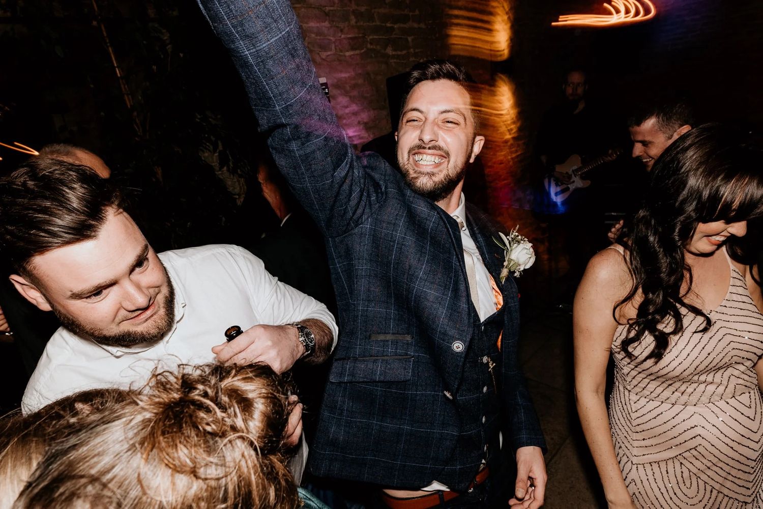 Lively wedding reception dance floor with guests celebrating in a dimly lit venue with ambient lighting.