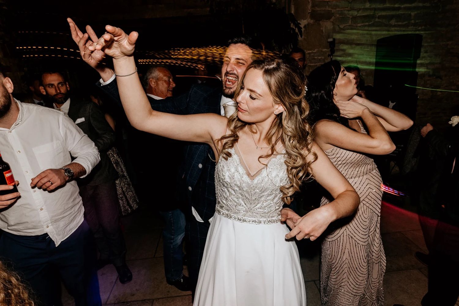 Wedding guests dancing joyfully on a dark dance floor at a reception celebration.