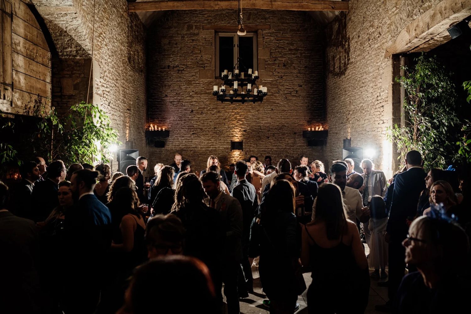 A low-lit stone-walled reception venue with guests mingling at a formal evening event.
