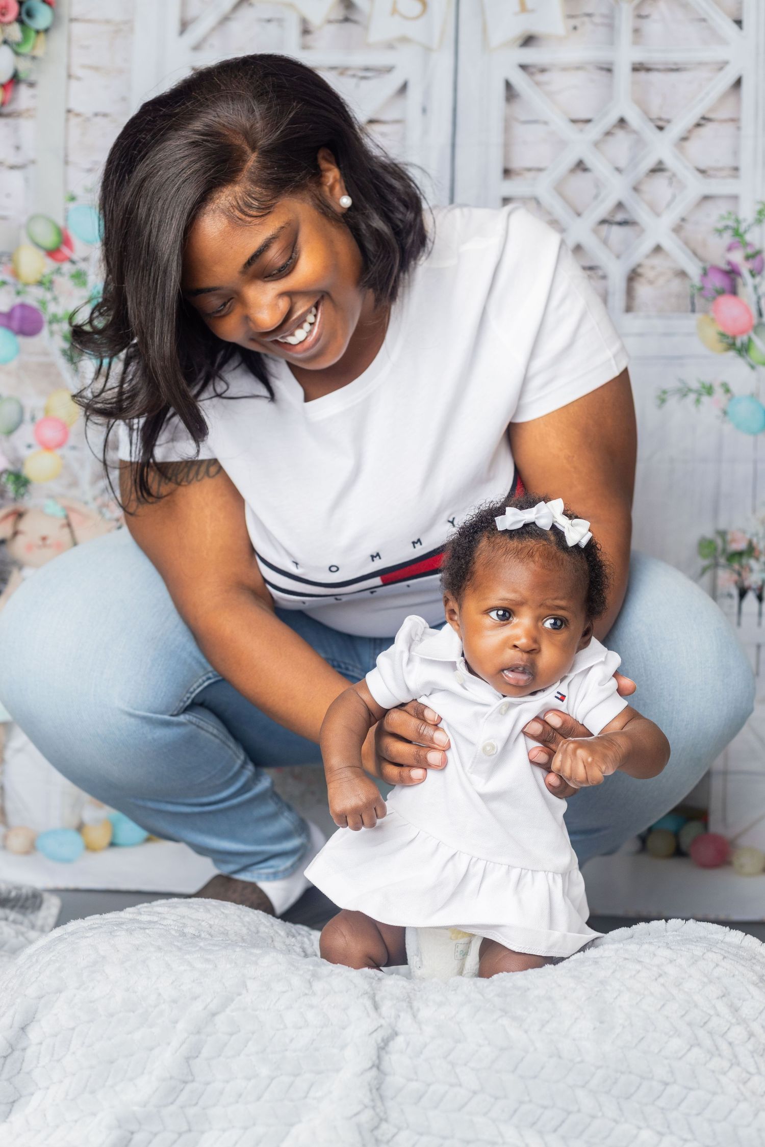 Sweet moment between parent and baby in white dress against floral backdrop.