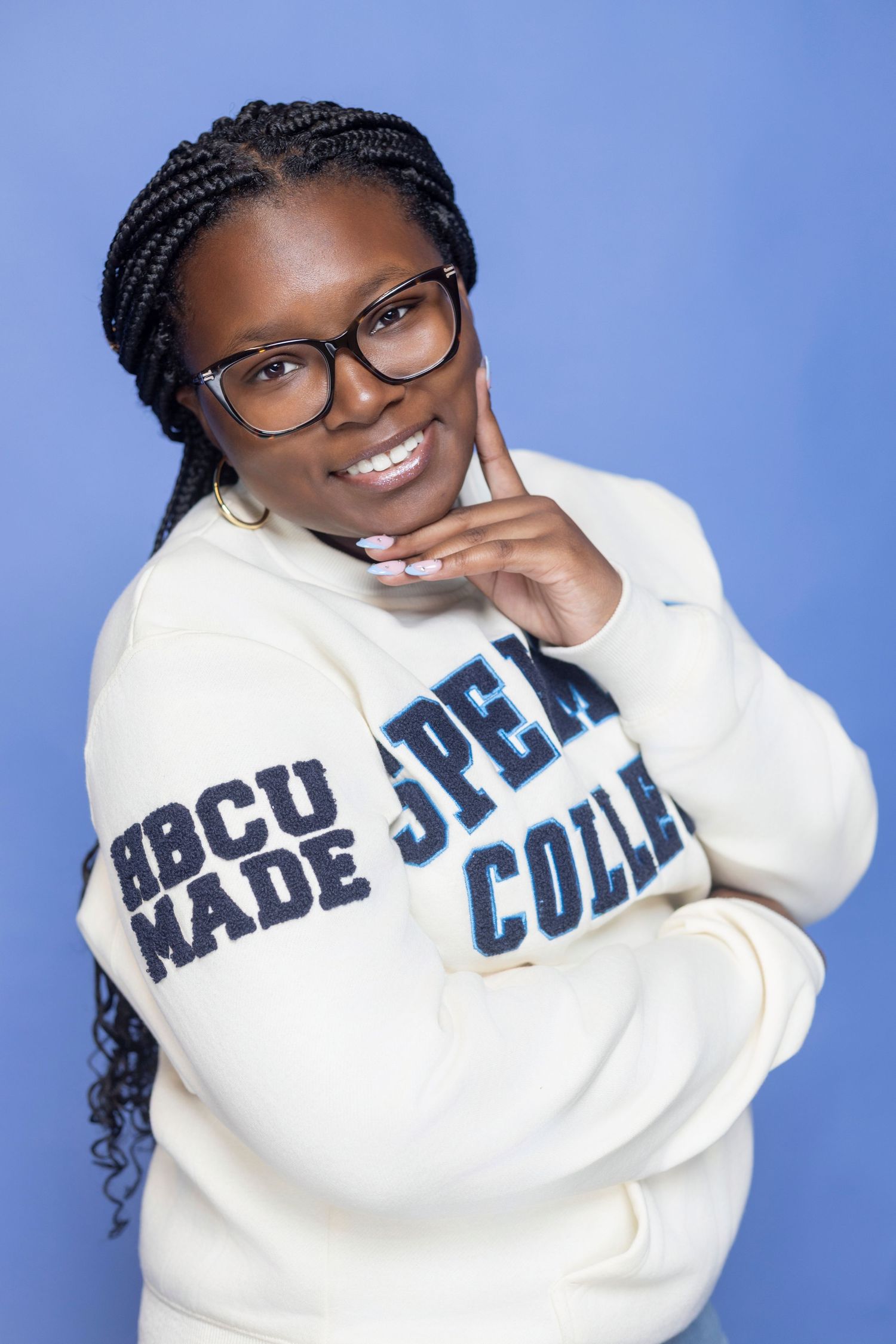 Student wearing college sweatshirt poses playfully against blue background.