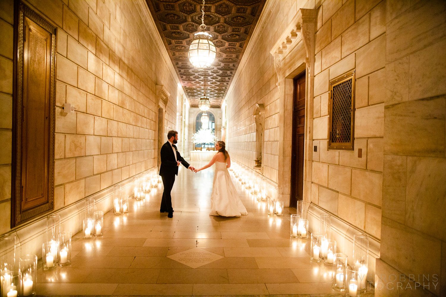 A long hallway with stone walls illuminated by string lights and pendant lamps creating a warm, romantic atmosphere.