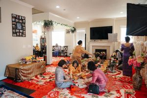 Indoor gathering with people sitting on red carpet near fireplace enjoying food during a casual party celebration.