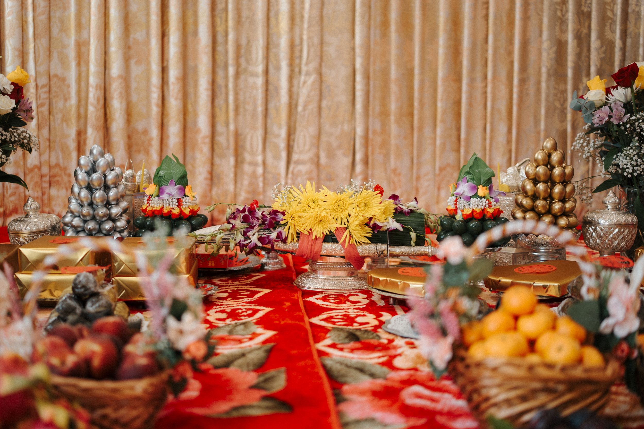 Elegant party dessert table with a red tablecloth features diverse sweets, fruits, and decorative arrangements.