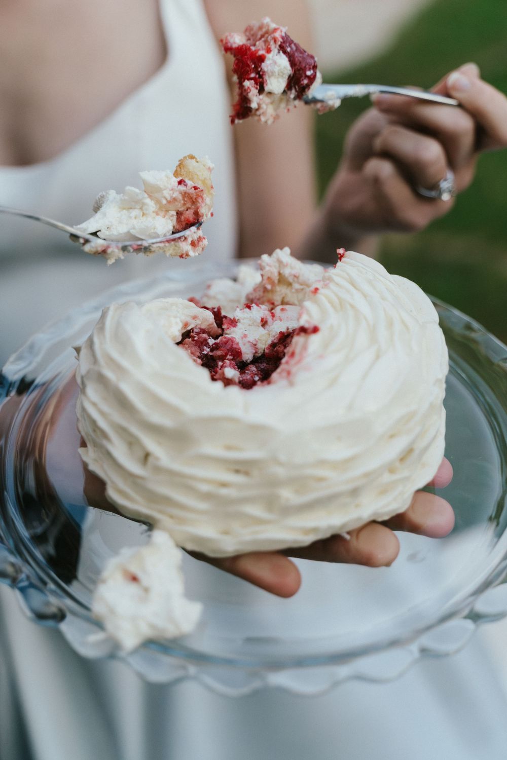 Bride holding a small white frosted red velvet wedding cake on a glass plate with a bite taken out of it.