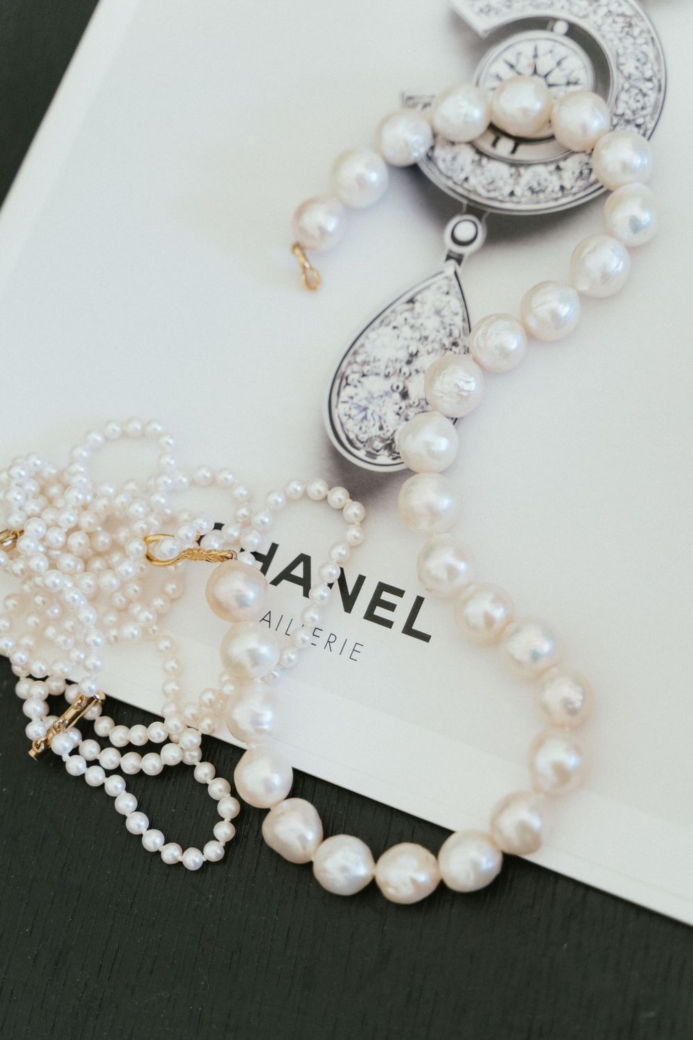 Elegant pearl necklaces and crystal earrings displayed on a Chanel jewelry catalog book.