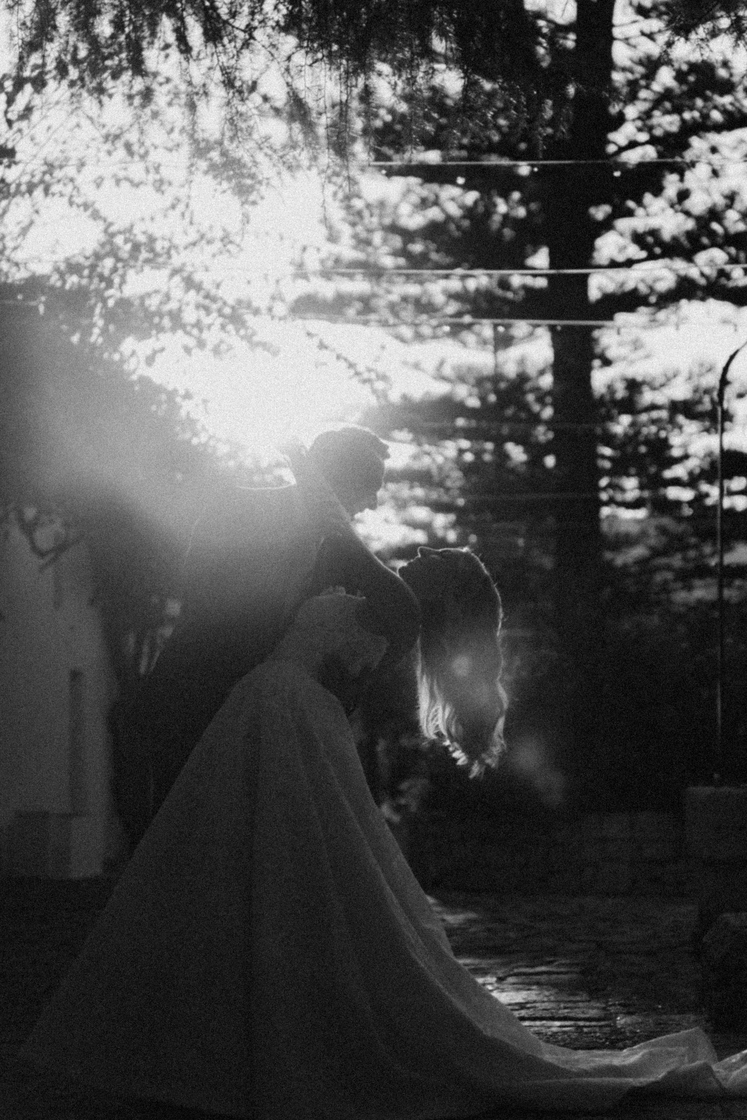Two silhouettes sit together against a dramatic sunset sky creating a romantic backlit scene in nature.