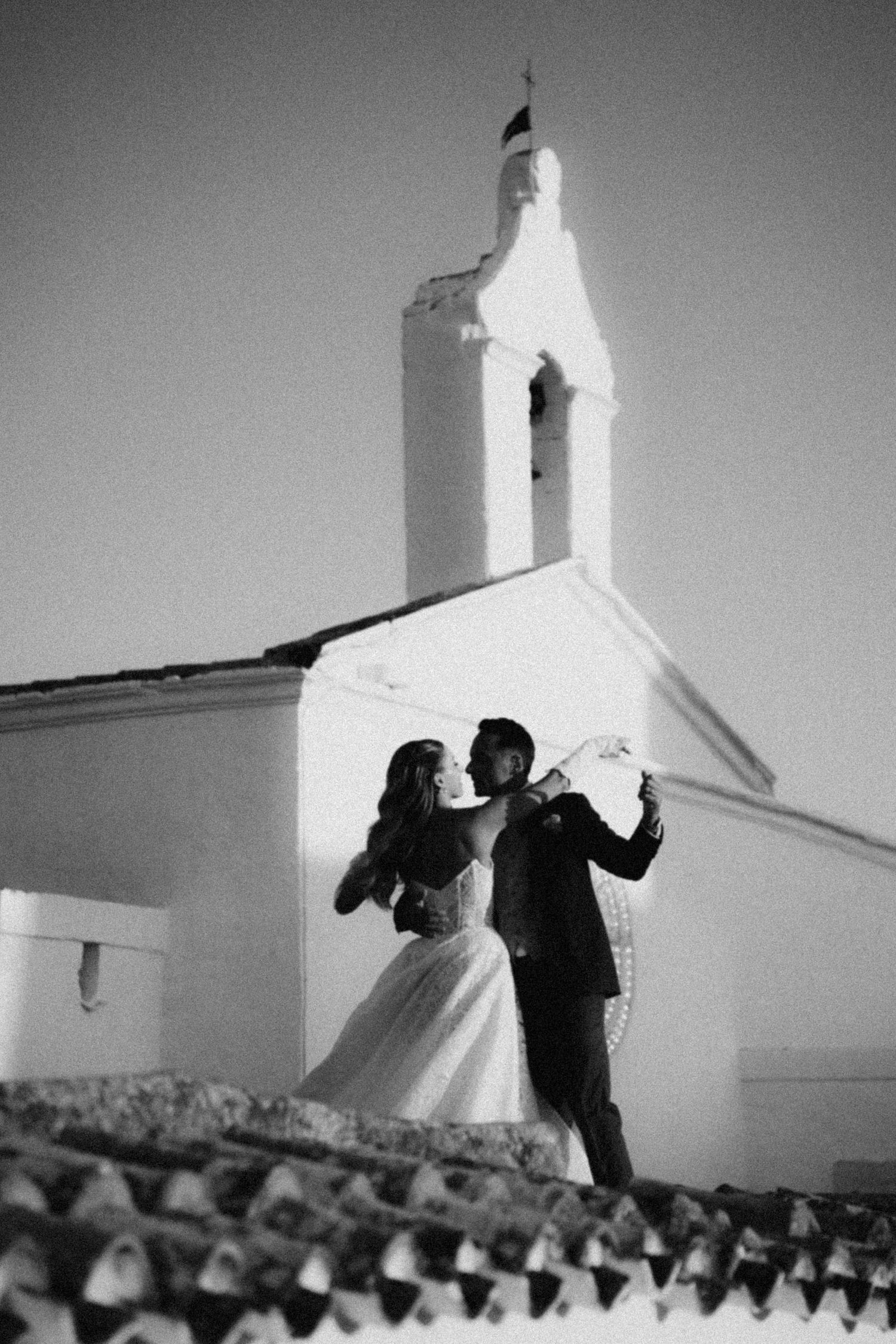 Two people silhouetted against a white church steeple in a dramatic black and white composition.