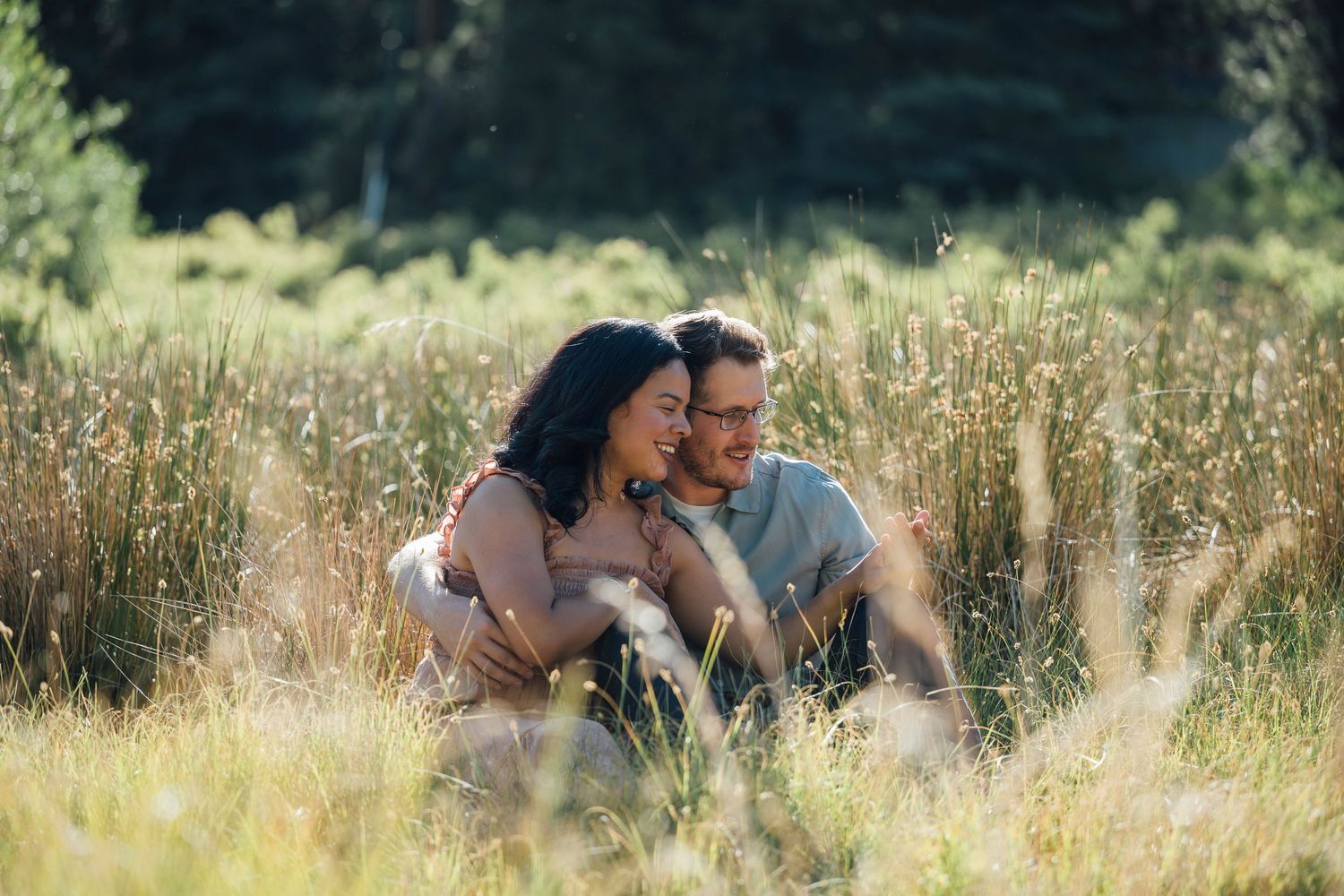 Two people share an intimate moment in a sunlit field of tall golden grass and wildflowers.