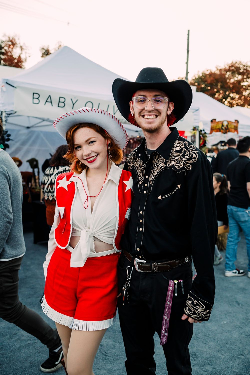 Couple in western-themed outfits at an outdoor festival with a red and black color scheme.