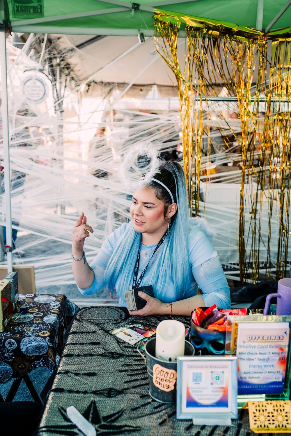 Blue-clad attendant serving treats at a festive event booth decorated with gold tinsel and party supplies.
