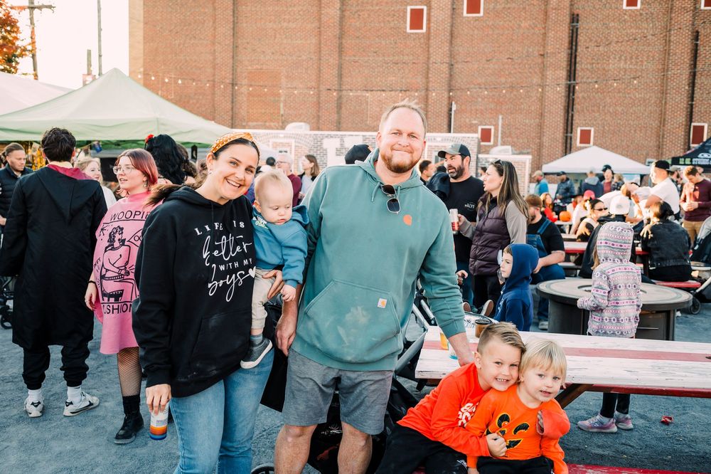 A crowd gathers at an outdoor market or festival with colorful displays and brick buildings.