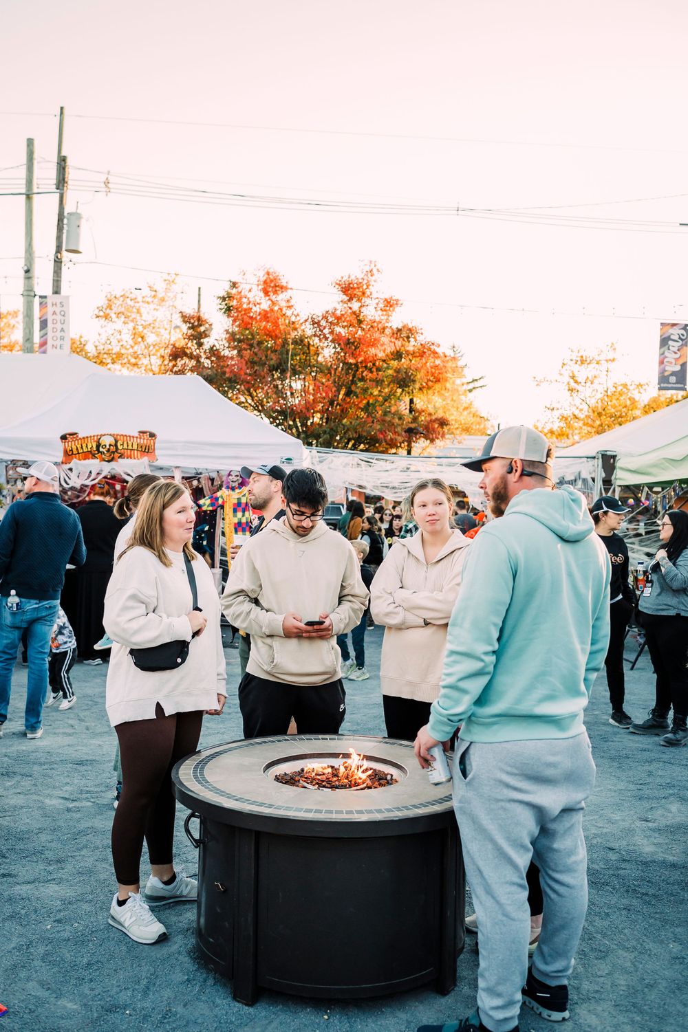 Group gathered around outdoor fire pits during evening autumn festival.