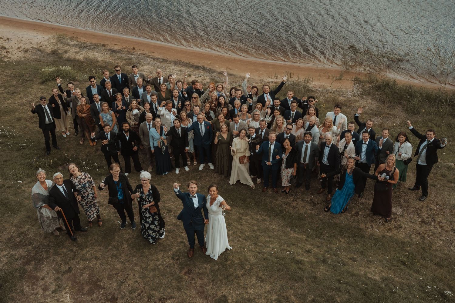 Wedding party enjoys a candid moment together in golden sunlight on grassy hillside.