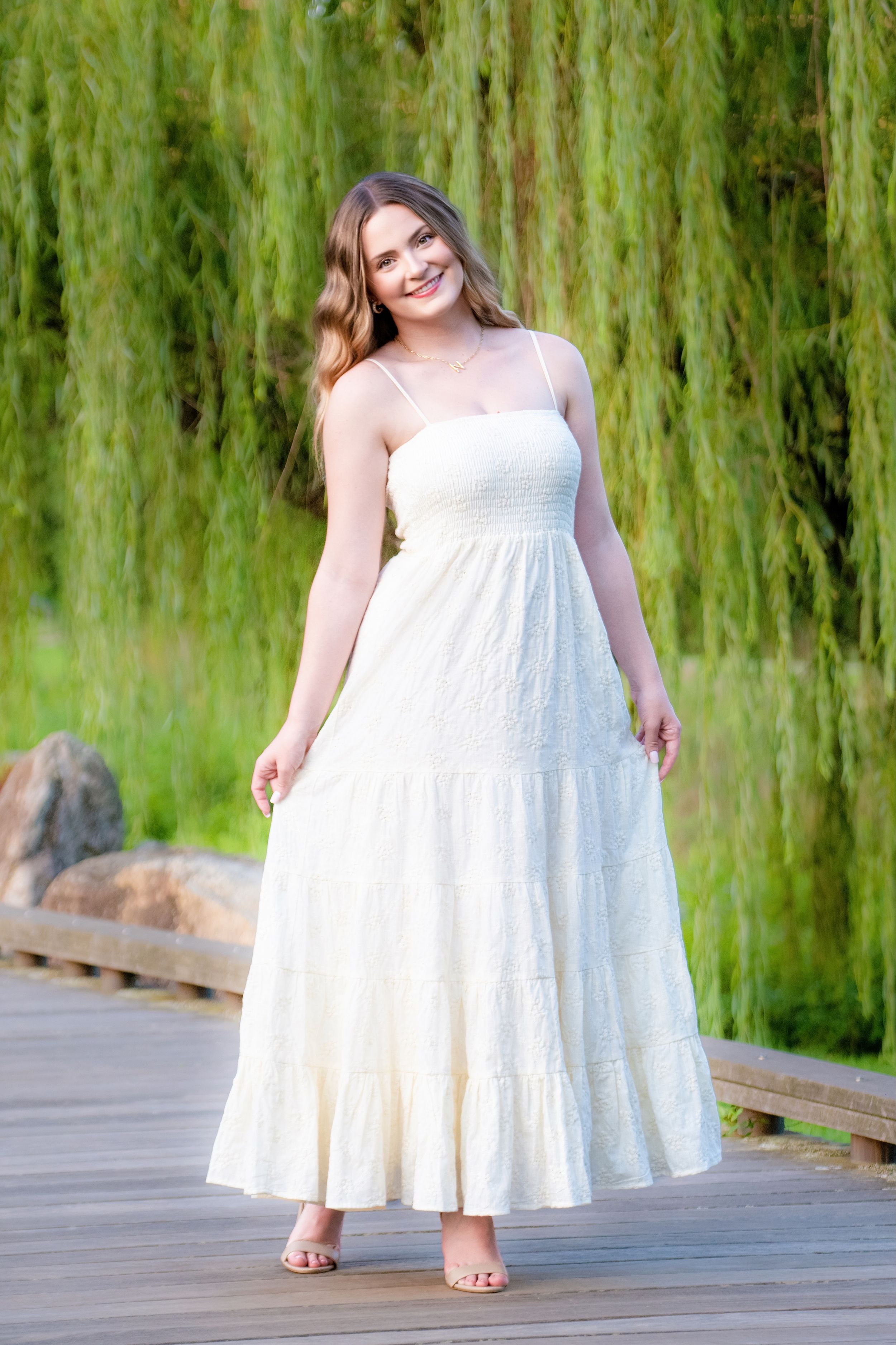 A sequence of photos showing a white eyelet summer dress with a flowing skirt against a green willow backdrop.