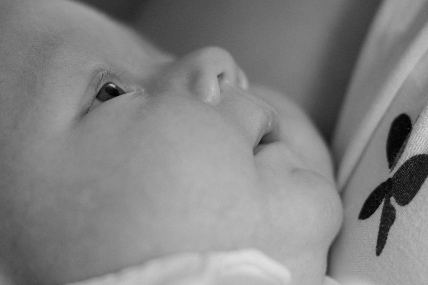 Close-up black and white photo of a newborn baby's face looking upward with soft features.