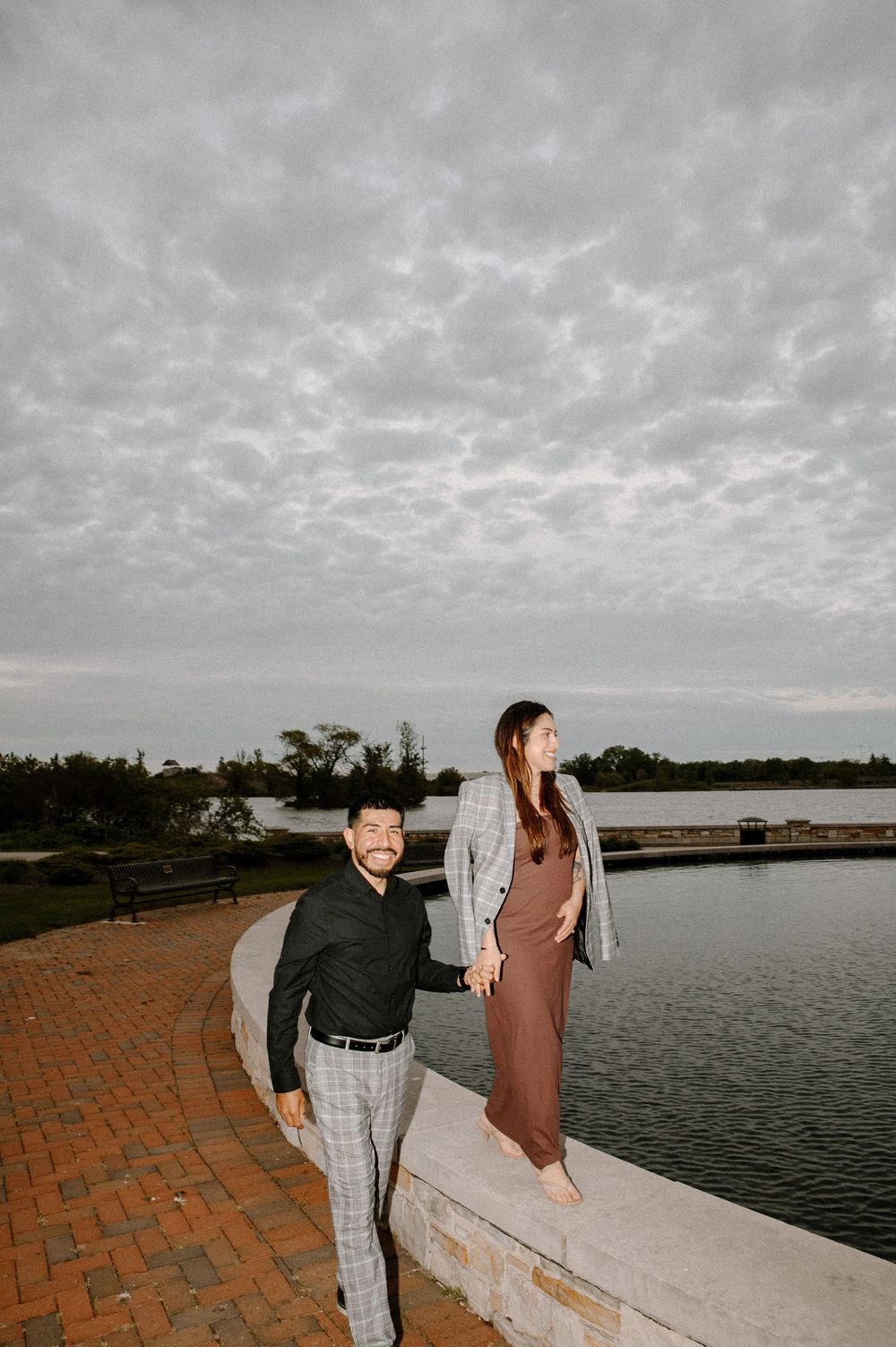 A romantic lakeside scene with a couple by brick paving and water under cloudy skies.