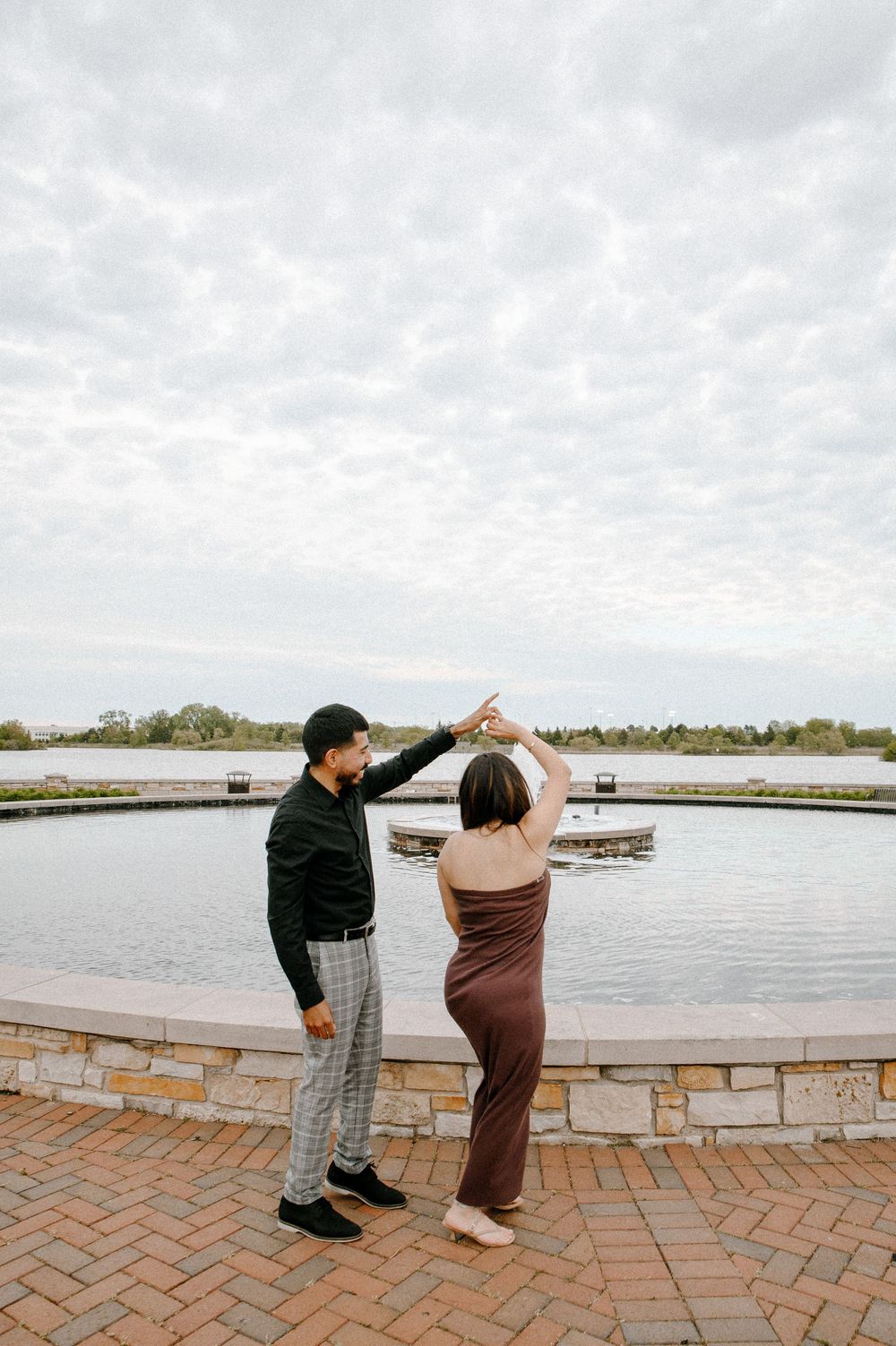 Two people point and gesture excitedly near a waterfront walkway on a cloudy day.