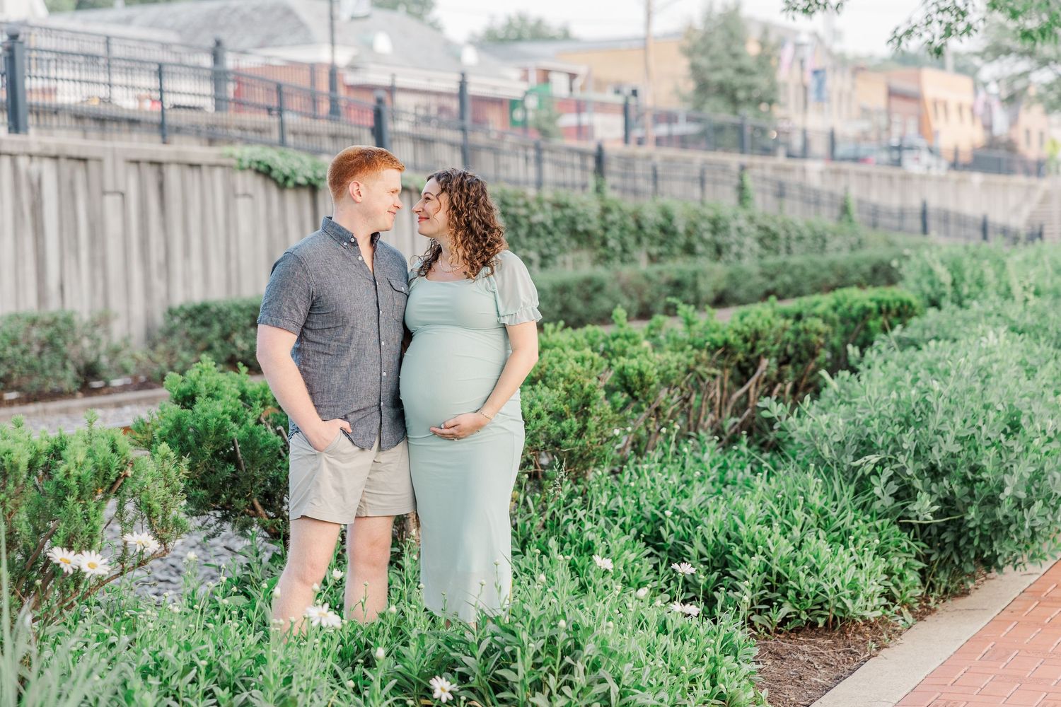 A maternity photography session along railroad tracks with urban buildings in the background.