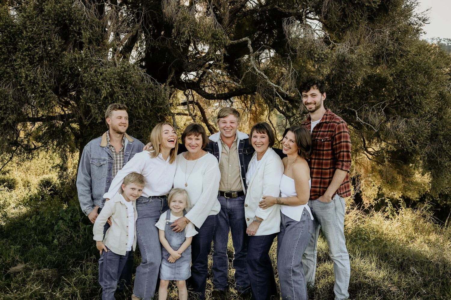 A family stands together in a grassy meadow wearing coordinated blue and white outfits during a sunny outdoor photo session.