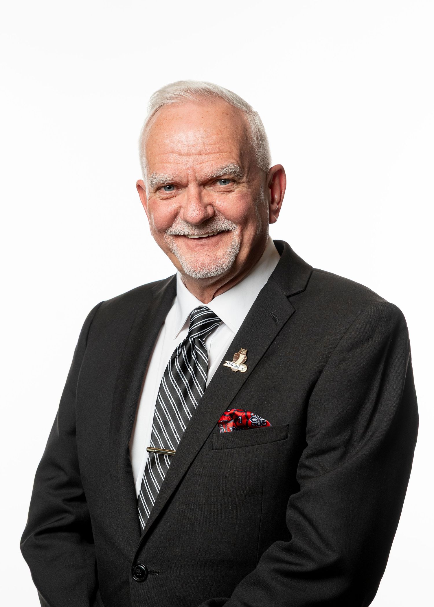 Professional headshot portrait of someone in a dark suit with striped tie and red pocket square against white background.