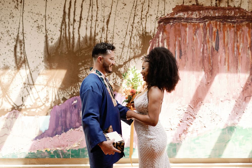 Bride and groom sharing first look moment in front of colorful abstract painted wall.