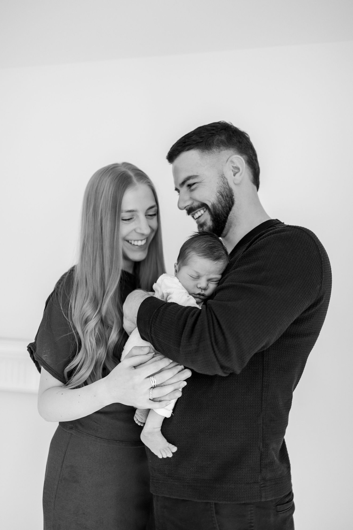 Black and white photo series showing loving parents cradling and smiling with their newborn baby in casual outfits.