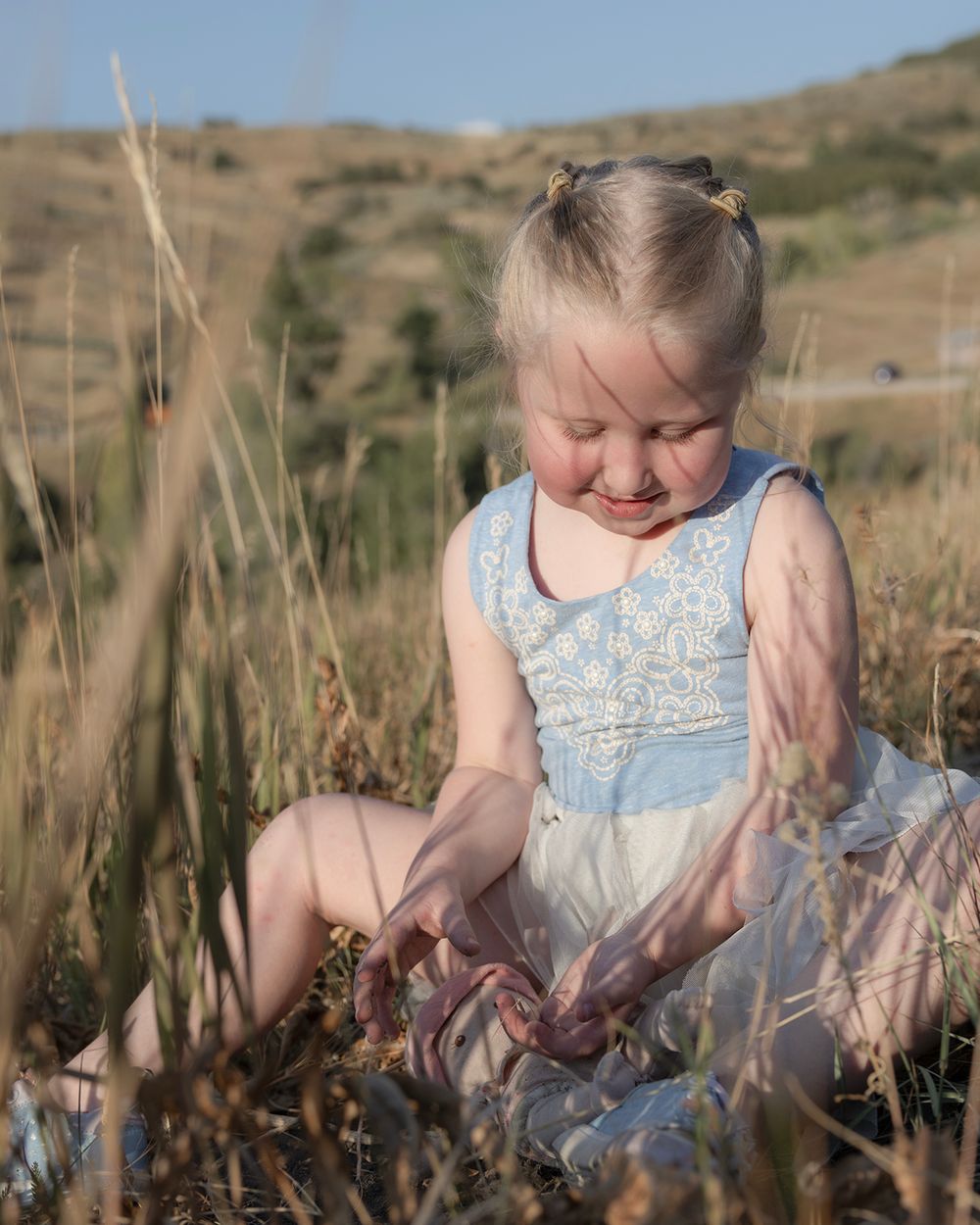 Candid moments in a blue dress playing in a golden field at sunset.
