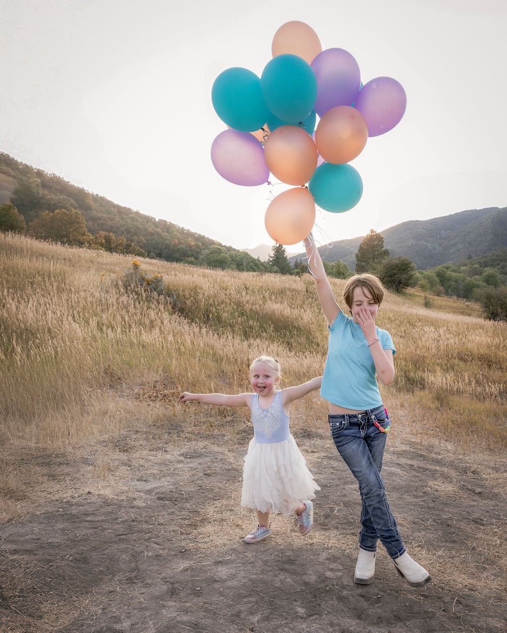 Playful scene with colorful balloons in a mountain field at sunset.